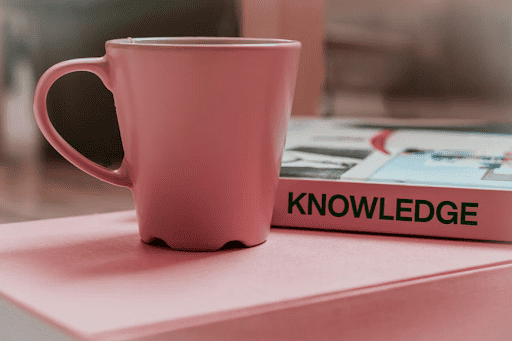 Pink coffee mug next to a book titled “Knowledge”