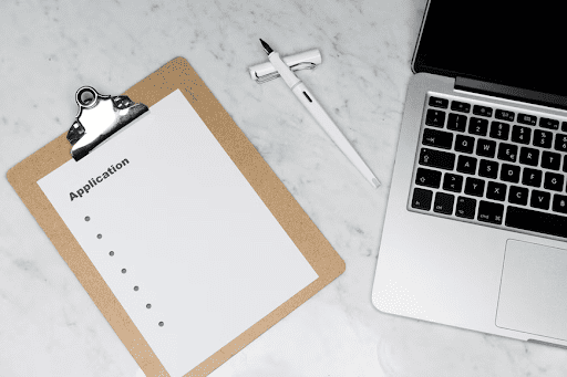 Application form on a clipboard next to a laptop and pen
