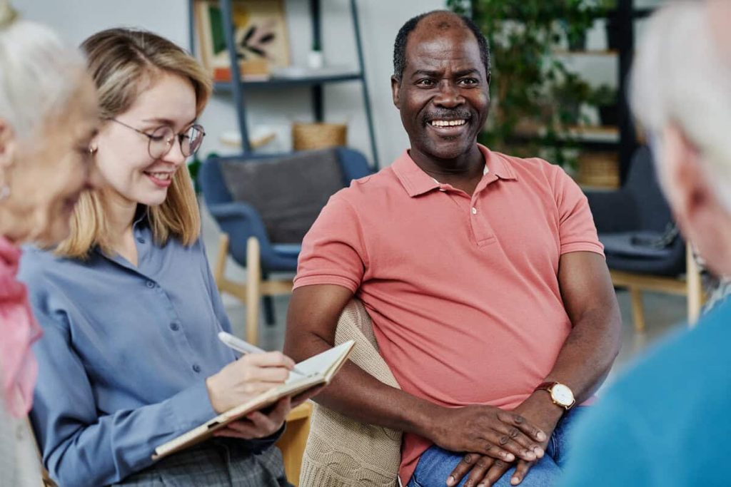 Smiling man in a support group meeting with a counselor taking notes
